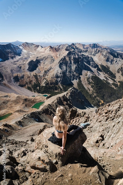 Fototapeta A woman sitting at the peak of Mount Sneffles with the Blue Lakes in the distance. 