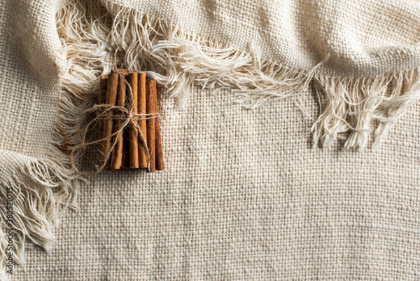 Fototapeta A set of cinnamon sticks tied with natural jute string on a tablecloth with fringe. Horizontal image with space for text.