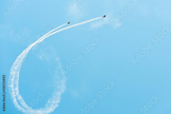 Fototapeta Planes doing aerial acrobatics and dropping smoke in a curved shape on a clear blue sky with copy space.