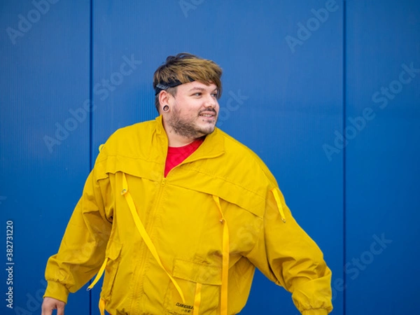 Fototapeta Hombre joven con chaqueta amarilla posando en una pared azul