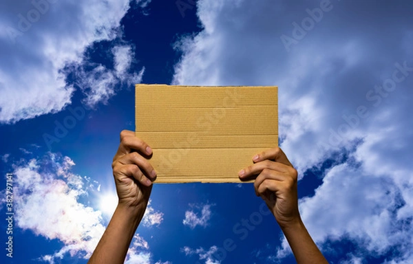 Fototapeta Hands hold a piece of cardboard where you can write anything, with a beautiful background of a cloudy blue sky