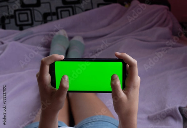 Fototapeta Phone with green screen, horizontal. With fingers on the screen. Gaming. Location - Limbazi, Limbazu novads, Latvia. Shoot date - 10/04/2020.