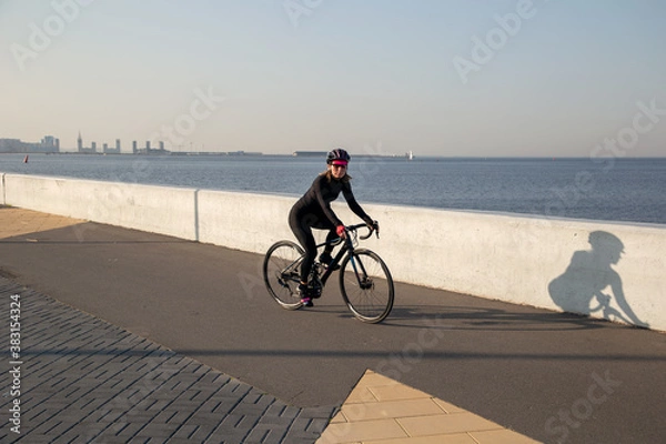 Obraz A woman rides a bicycle along the embankment. Riding a bicycle. Outdoor sports. Embankment of the Gulf of Finland Russia St. Petersburg.Cycling workout