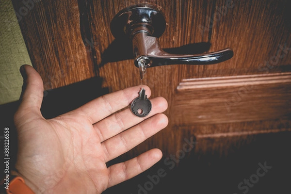 Fototapeta A man holds in his hand a small light broken key against the background of a door lock.