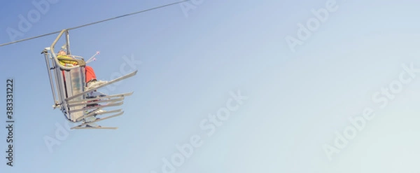 Fototapeta Banner with big group of skiers in ski lift, going uphill in a ski resort at blue and yellow clean gradient sky during sunset with copy space for text.