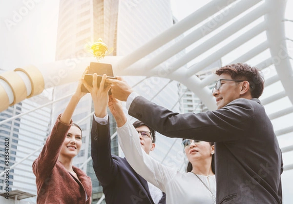 Fototapeta The best team helped each other reach their goals target to success. The hand of a business man and business women pick up the trophy and celebrate together. Asian Teamwork of successful concept