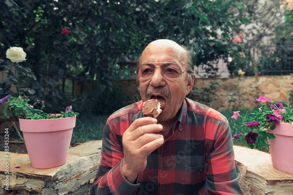 Fototapeta Close-up Portrait of senior man eating ice cream. Elderly man eating ice cream on stick in the backyard.