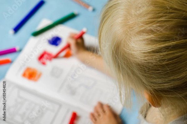 Fototapeta Homeschooling a girl first grade student doing homework with a notebook and felt tip pen at the table at home.