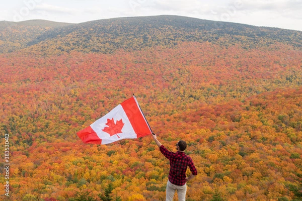 Obraz Autumnal view of a man with a lumberjack shirt holding a Canadian flag in the Mont-Megantic national park, Canada