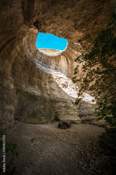 Fototapeta A hole from which the sun's rays and the sky are visible outside of an underground cave, an abnormal natural phenomenon in the rocks in the Crimea