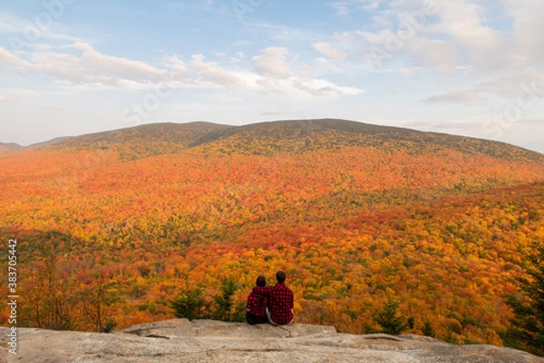 Obraz Back view of a young couple sitting on the edge of a cliff and admiring the autumnal colours in the Mont-Megantic national park, Canada