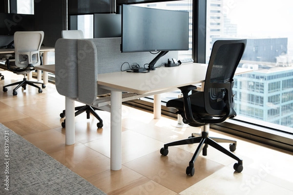 Fototapeta Modern flexible office work space interior fitout rows desks chairs floor cieiling windows T5 lights computer stations screens cityview	