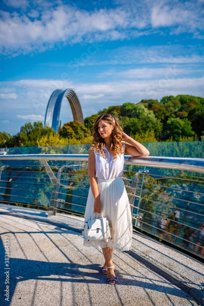 Obraz a girl in a white dress is walking under the rainbow building on a summer day. 