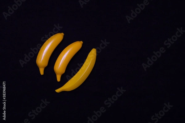 Fototapeta Three bananas on a dark background. Plastic toy