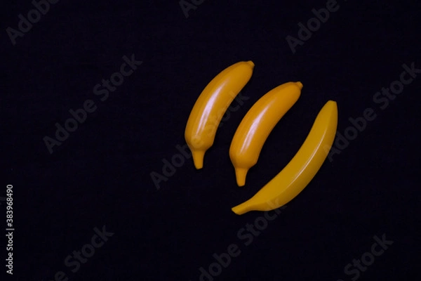 Fototapeta Three bananas on a dark background. Plastic toy