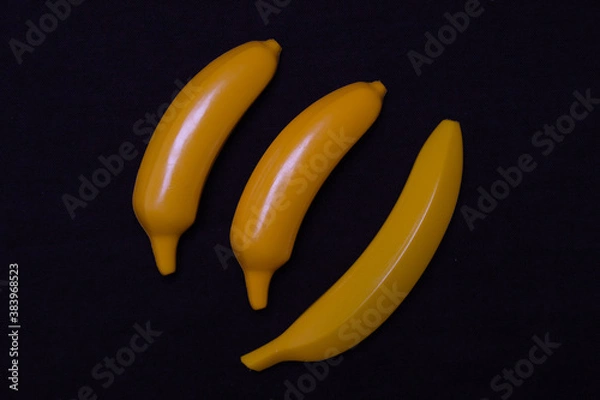 Fototapeta Three bananas on a dark background. Plastic toy