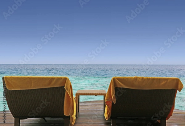 Fototapeta two chairs with towels and table on the wooden bungalow terrace overlooking the ocean