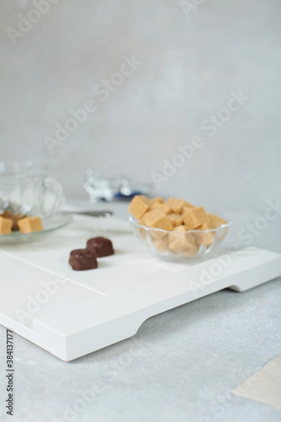 Obraz sweet still life of brown cane sugar in a sugar bowl and chocolates on a white tray. soft focus and highly blurred background. stylish background concept
