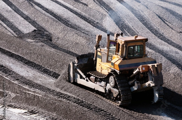 Fototapeta The bulldozer harrows the mountain soil, and then removes the top layer with an industrial bucket. Extraction of minerals in mountainous areas, in Siberia (gold mining)