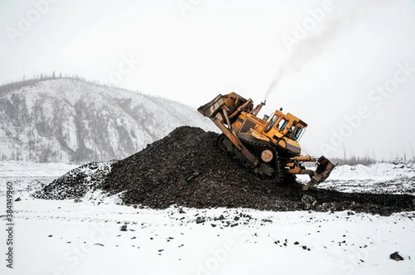Fototapeta A bulldozer in a mountainous area in an industrial area shovels up a pile of mountain soil. Mining.