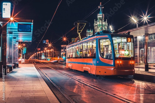 Fototapeta A modern tram stop in the center of Moscow with a tram. Night. Lanterns and city lights are on. In the background, a Stalinist skyscraper on Kotelnicheskaya embankment. Translation: Stop. Thank you