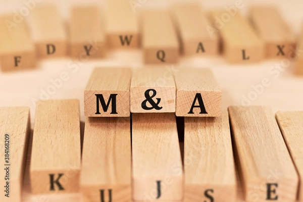 Fototapeta Word M and A Merger and Acquisition on wooden blocks beige background top view, scattered cubes around random letters