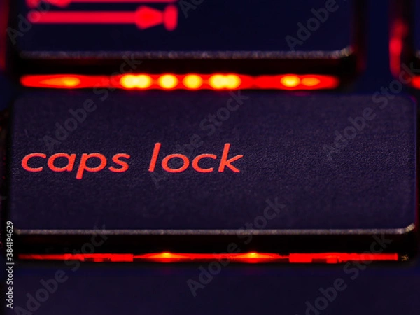Obraz Black keyboard caps lock key with red backlight. 