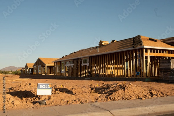 Obraz A new house construction with the wood frame before the siding  stands next to an empty dirt lot with a sold sign, horizontal view.