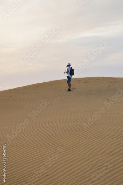 Fototapeta Young man on vacation walking through the desert dunes.