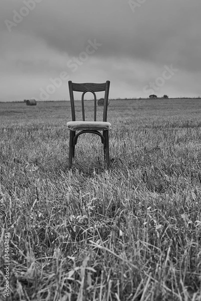 Fototapeta One old chair stands in a mown field against a cloudy sky.