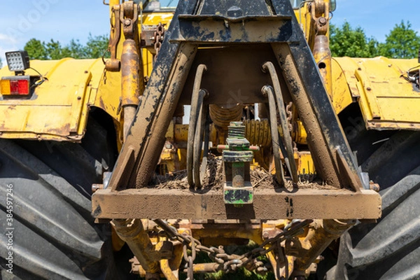 Fototapeta Closeup of a yellow tractor with heavy wheels in a field with trees in background