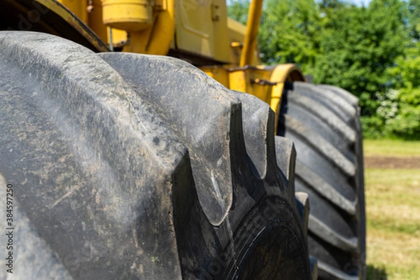 Fototapeta Closeup of a yellow tractor with heavy wheels in a field with trees in background