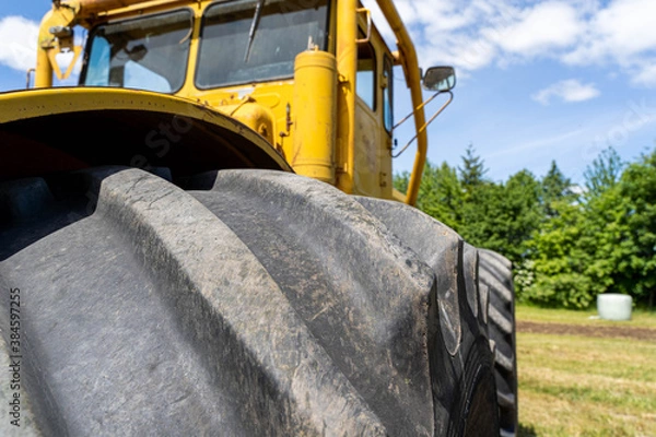 Fototapeta Closeup of a yellow tractor with heavy wheels in a field with trees in background