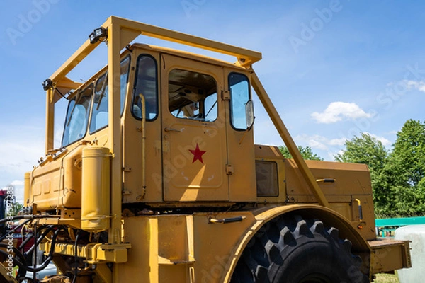 Fototapeta Closeup of a yellow tractor with heavy wheels in a field