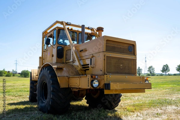 Fototapeta Closeup of a yellow tractor with heavy wheels in a field