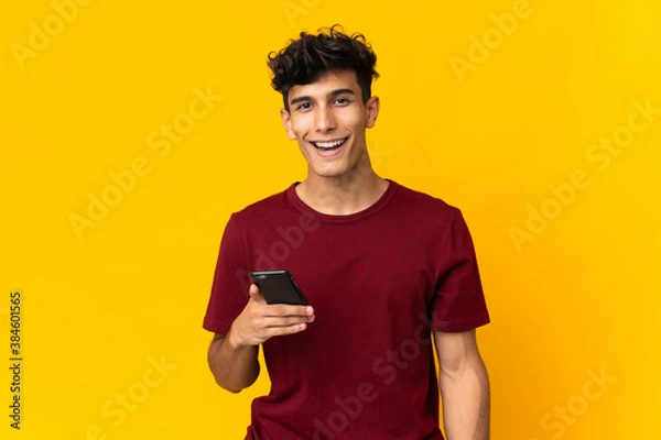 Fototapeta Young Argentinian man isolated on yellow background using mobile phone