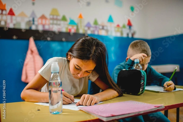 Fototapeta Elementary schoolchildren writing at the desk in the classroom.