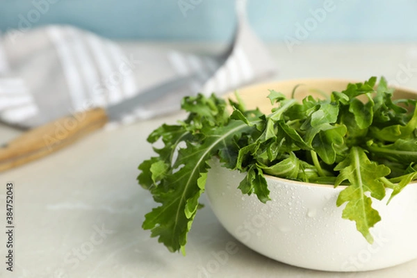 Fototapeta Fresh arugula in bowl on light grey table. Space for text