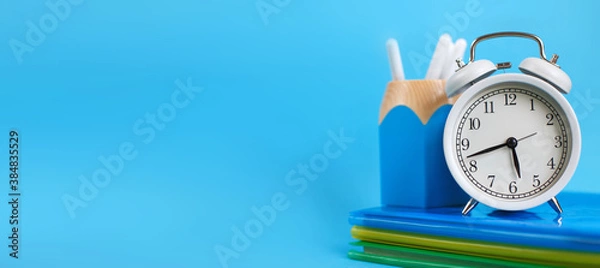 Fototapeta Textbooks and alarm clock on a blue background. Back to school. Concept Education or business. banner