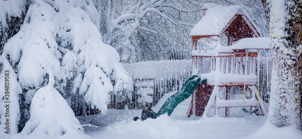 Fototapeta Young boy  using a slide on a backyard play set in the middle of a snowy blizzard.
