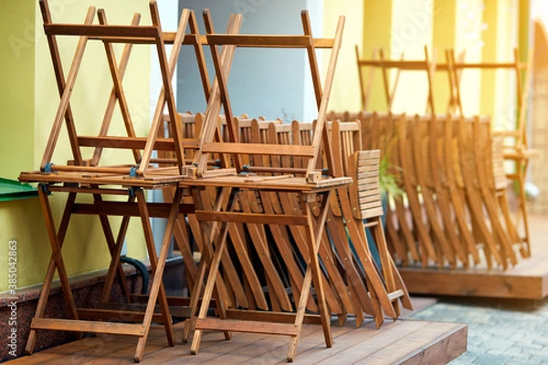 Fototapeta Wooden furniture folded on summer terrace before the opening of the restaurant. Street cafe before opening. Pile of wooden chairs and tables on summer terrace of street cafe.