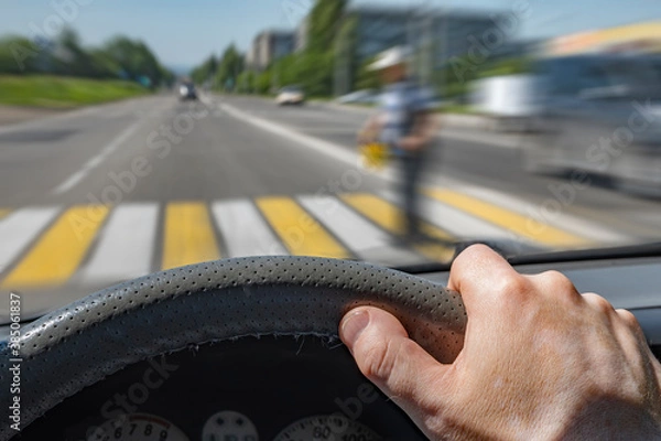 Fototapeta the driver hand on the steering wheel of a car moving at high speed and passing a pedestrian crossing with the risk of hitting a person