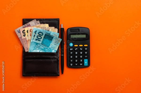 Obraz Brazilian money in wallet, with notepad, pen and calculator. Finance and salary concept. Economy of Brazil. Orange background