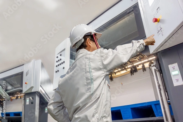 Obraz 印刷工場で枚葉オフセット印刷機を操作する作業着を着た男性オペレーターの後ろ姿の上半身。