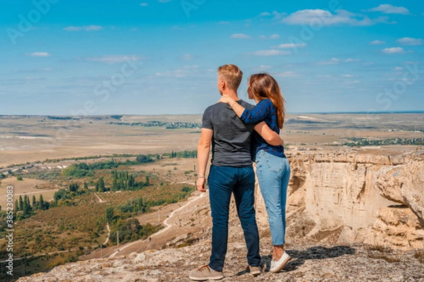 Fototapeta Rear view of a romantic couple a man and a woman standing on the edge of a cliff on a White rock in Crimea with a view of the rural landscape