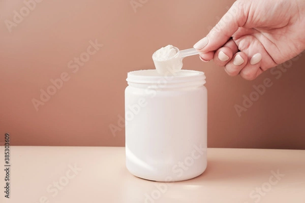 Fototapeta hand holding scoop of fish collagen. collagen peptides in container or jar. powder for mixing drink. Healthcare supplement concept. collagen for skin and joints .