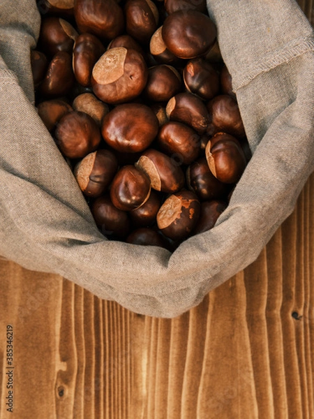 Fototapeta Vertical shot of chestnut in the linen bag on a wooden table 
