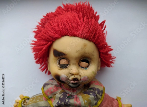 Obraz scary and old battered clown doll with burnt face and red hair on a white background