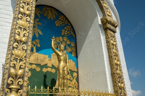 Fototapeta A golden statue of Buddha, standing with a raised hand, located in a niche, surrounded by traditional Buddhist designs