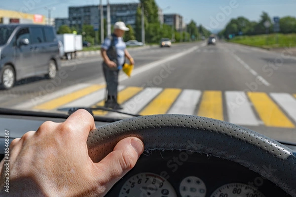 Fototapeta driver hand on the steering wheel of a car against the background of a pedestrian passing through a Zebra crossing